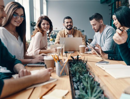 Doing business. Group of young modern people in smart casual wear discussing something and smiling while working in the creative office Doing business. Group of young modern people in smart casual wear discussing something and smiling while working in the creative office